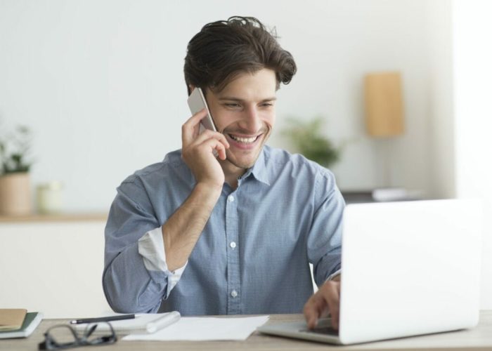 Happy Entrepreneur Talking On Cellphone Sitting At Laptop In Office